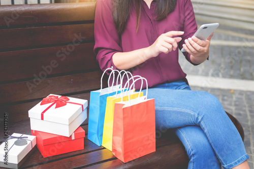 Woman look at mobile phone with paperbags in the mall while enjoying a day shopping.