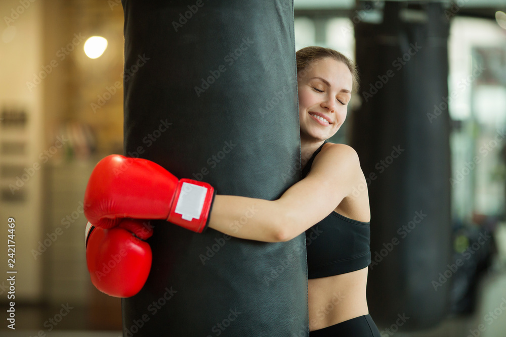 beautiful young girl hugs a punching bag in the gym
