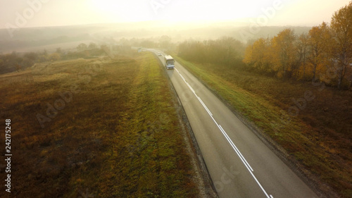 Bus traveling on the asphalt road in a rural autumn landscape at sunset