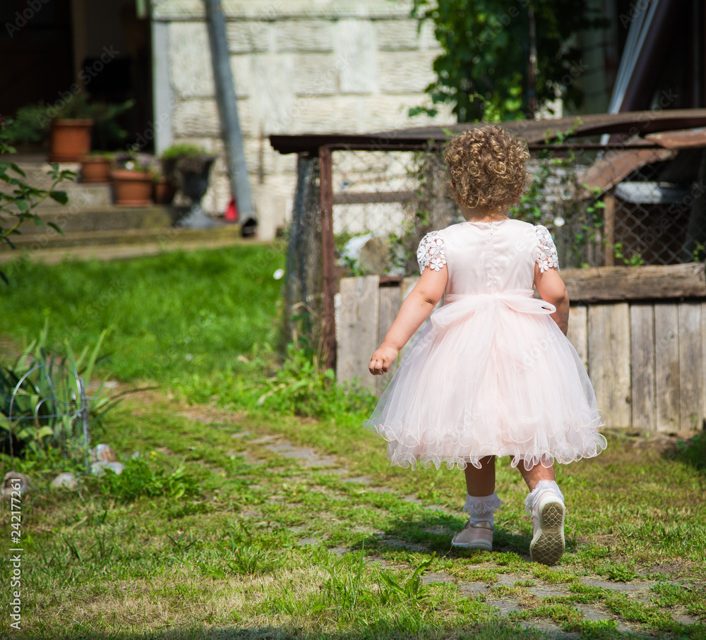 Cute little girl in a pink dress playing in a garden