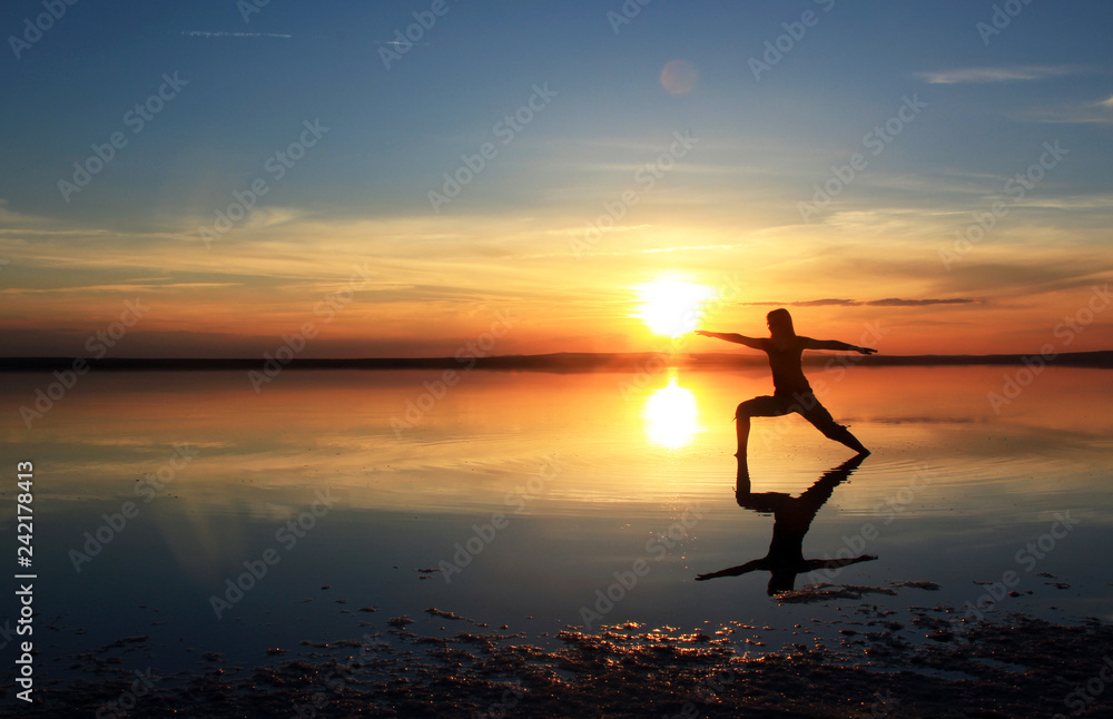 silhouette of young woman doing yoga on the beach at sunset