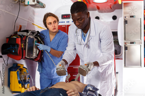 Obraz na płótnie attentive afro paramedical using defibrillator for providing medical care to pat
