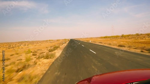 Point of view shot of red car driving along the straight highway to the ran of kutchh white desert in gujarat india. The long straight road with desert on both sides is a landmark to the amazing drive photo