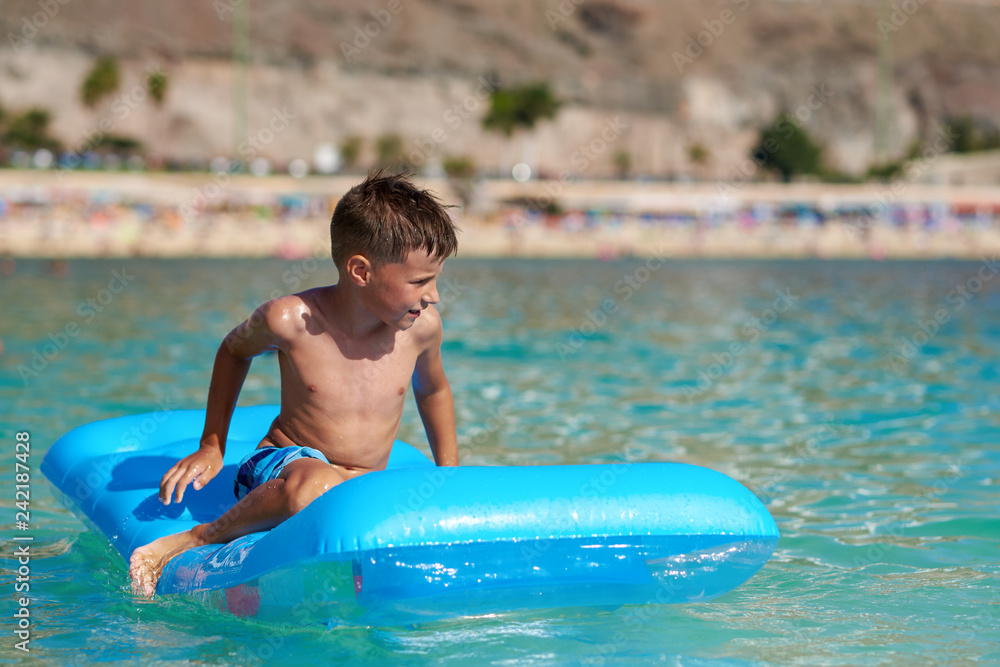 European boy is swimming in the sea on the blue air mattress. He is happy and enjoying his holidays.