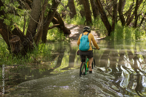 Female, baby boomer cycling through a flooded section of the bike path along the Clutha River near Clyde, New Zealand.