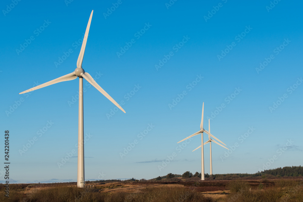 A scene depicting renewable energy, clean energy, and green energy with a group of three wind turbines under a blue sky in Northern Ireland