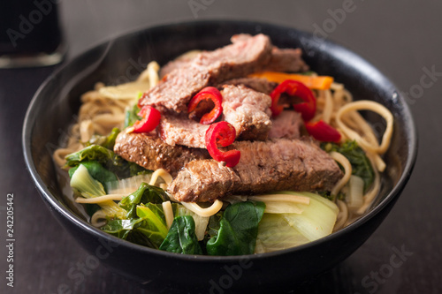 Close-up of a bowl of homemade ramen topped with slices of steak and fresh red chilli