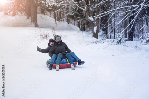 young guy and a girl ski tubing in the winter ride down a hill