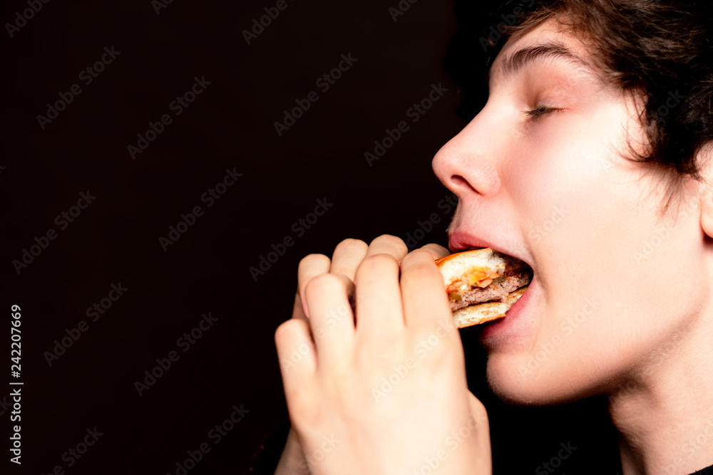 closeup photo of mouth bite junk hamburger on dark background isolated b
