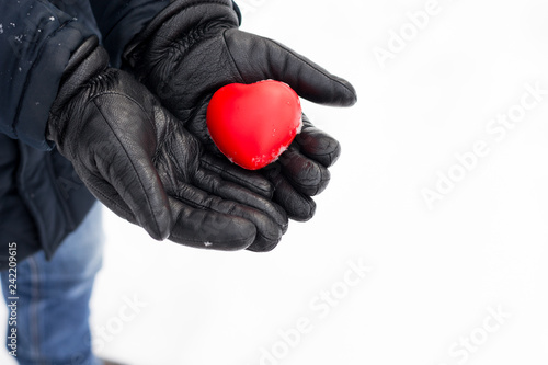 Man holds his heart in hand with lether gloves in winter snowy day. Copy space for text. Love and Valentine's day concept.