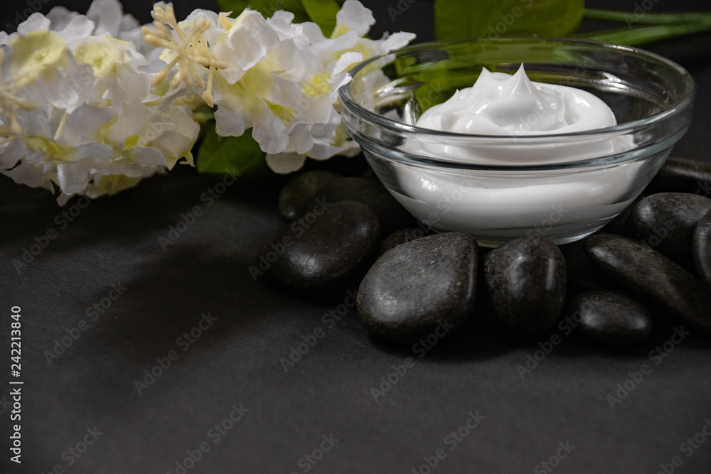 side view of natural skin care ointment in glass bowl on rock base with bouquet of white lilacs. side view of natural skin care ointment in glass bowl on rock base with bouquet of white lilacs.