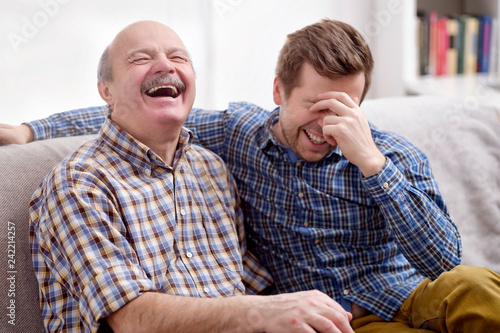Принти на полотні Father and son are sitting on the sofa in the living room and remember joke