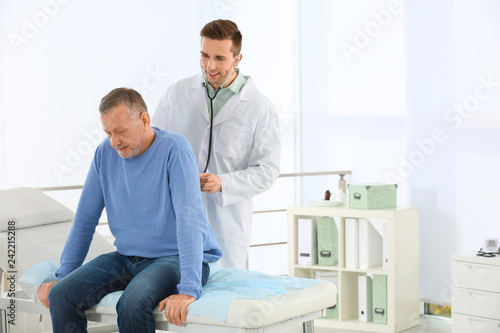 Doctor examining mature patient with stethoscope in hospital. Space for text
