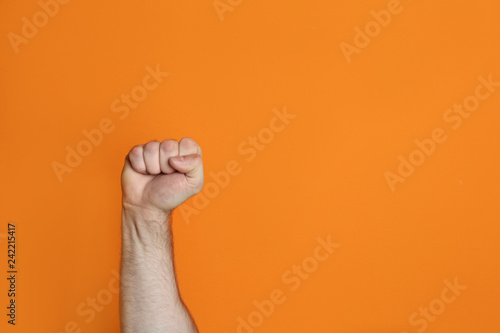 Young man showing clenched fist on color background. Space for text