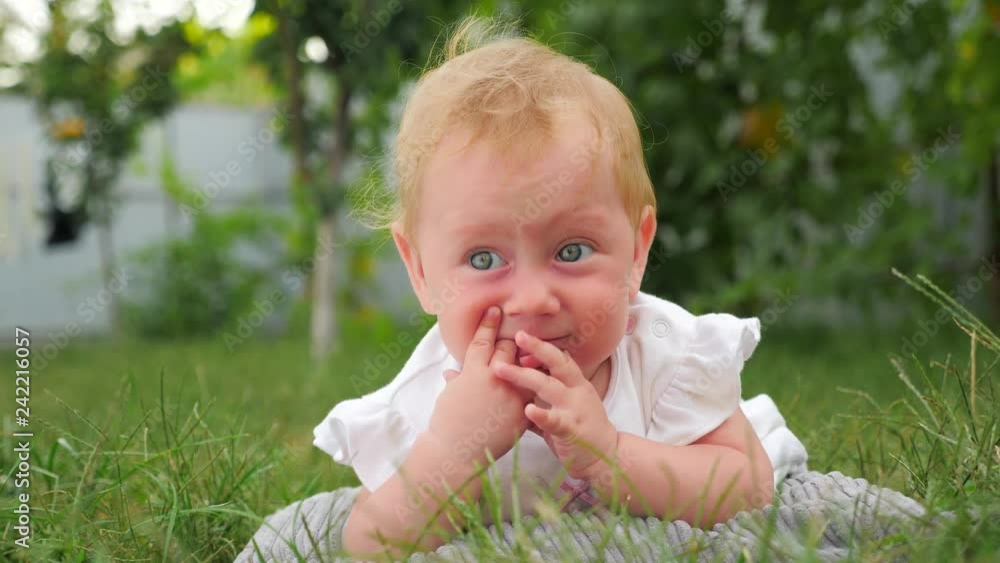 Baby teething background. Baby teething problems. Baby lying on green grass. Kid playing in the garden. Teeth are cutting through. Blue eyed girl smiling outdoor. Child in summer forest. Eco living. Baby teething background. Baby teething problems. Baby lying on green grass. Kid playing in the garden. Teeth are cutting through. Blue eyed girl smiling outdoor. Child in summer forest. Eco living.