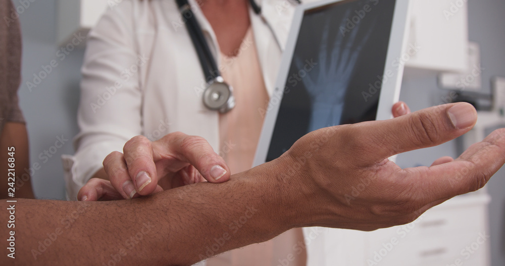 Obraz premium Close up of male patient hand and wrist with doctor explaining x ray on tablet. Tight view of senior doctor holding electronic pad with x-ray of patients wrist and hand