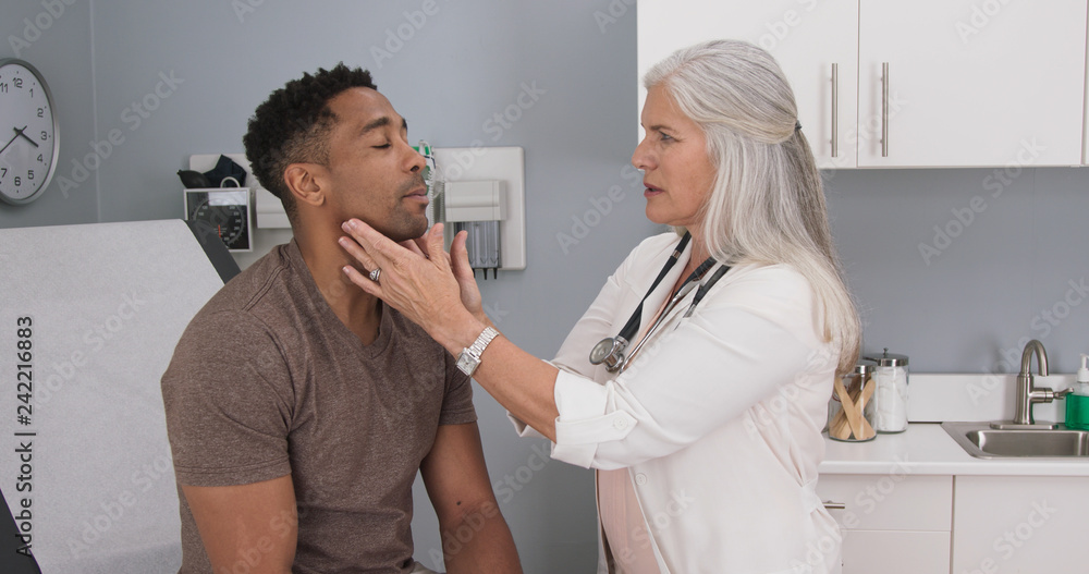 Portrait of senior medical doctor examining patients neck for swollen thyroid. Attractive black male having doctor checkup at health clinic - obrazy, fototapety, plakaty 