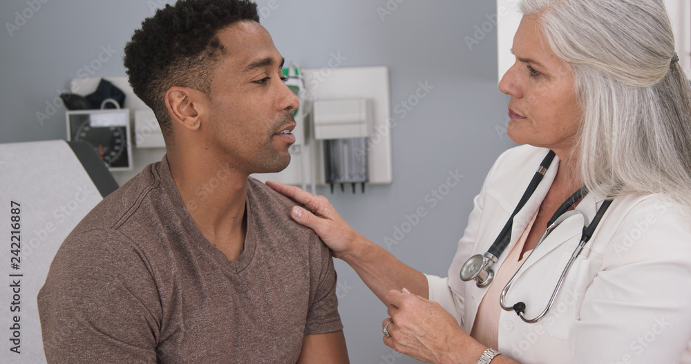 Close up of senior female doctor examining male patients neck. Portrait of attractive black male having doctor checkup at health clinic Close up of senior female doctor examining male patients neck. Portrait of attractive black male having doctor checkup at health clinic