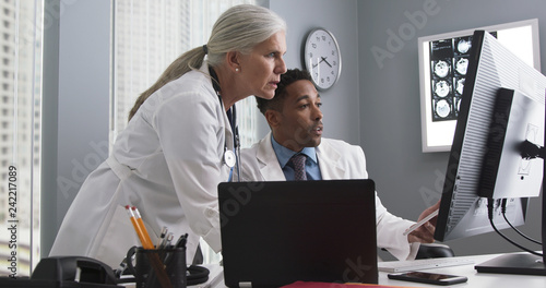 Millennial male doctor using tablet and looking at computer screen with colleague. Two medical doctors working inside office using technology