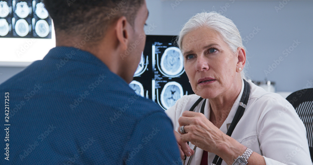 Obraz premium Young male patient talking to doctor about concussion indoors health clinic. Close up of female medical doctor discussing results from ct scan with patient