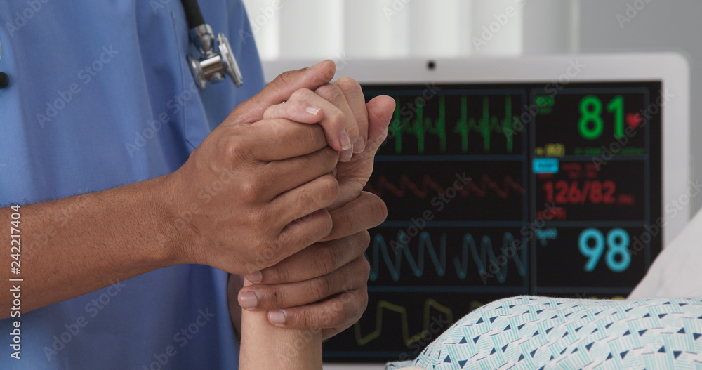 Portrait of registered nurse holding hand of sick patient in hospital bed. Closeup of black nurse hands holding white womans hand in bed Portrait of registered nurse holding hand of sick patient in hospital bed. Closeup of black nurse hands holding white womans hand in bed