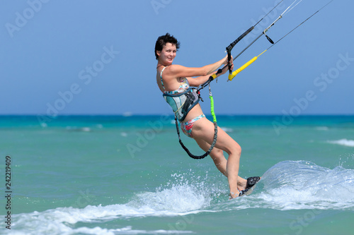 Kite surfing girl in sexy swimsuit with kite in sky on board in blue sea riding waves with water splash. Recreational activity, water sports, action, hobby and fun in summer time. Kiteboarding sport