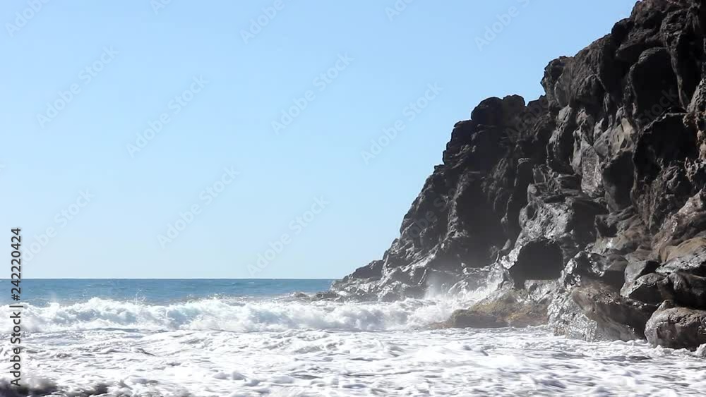 Rough sea with waves crashing on black rocks cliff on sunny day. Environment, climate change effects concepts Rough sea with waves crashing on black rocks cliff on sunny day. Environment, climate change effects concepts