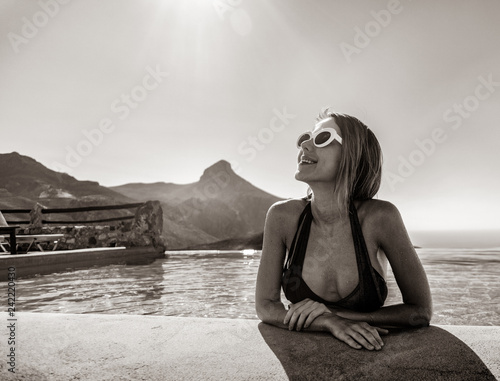 Young girl in bikini and sunglasses in a pool with mountains on background. Crete, Greece
