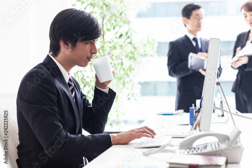 窓際のデスクでコーヒーを飲みながら仕事に取り組む男性会社員 Stock 写真 Adobe Stock