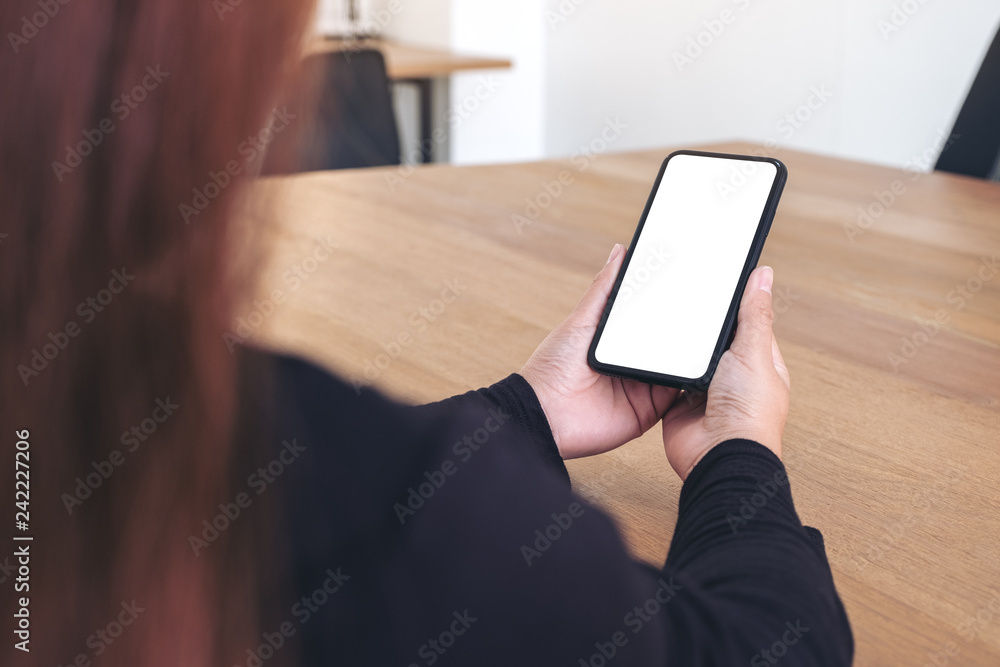 Mockup image of a woman holding black mobile phone with blank white screen on wooden table in office Mockup image of a woman holding black mobile phone with blank white screen on wooden table in office