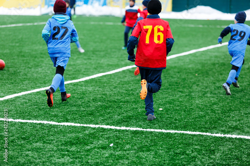 Boys in red and blue sportswear plays soccer on green grass field. Youth football game. Children sport competition, kids plays outdoor, winter activities, training