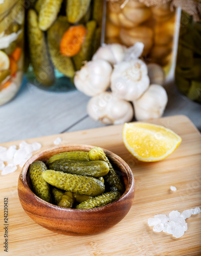 Bowl of pickled cucumbers and jars of pickled vegetables on wooden background