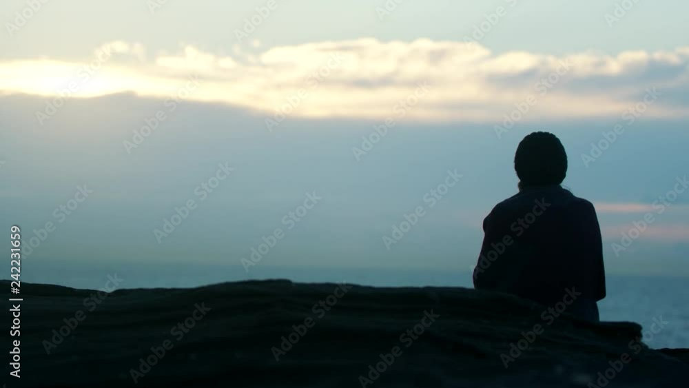 Woman Thinking and Watching Sunrise on Cliff, Wind Blowing Hair and Jacket Woman Thinking and Watching Sunrise on Cliff, Wind Blowing Hair and Jacket