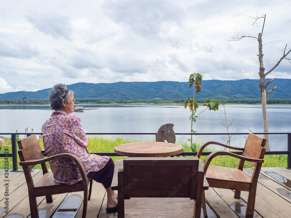 Elderly woman sitting on chair side the lake.