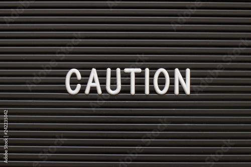 Black color felt letter board with white alphabet in word caution background