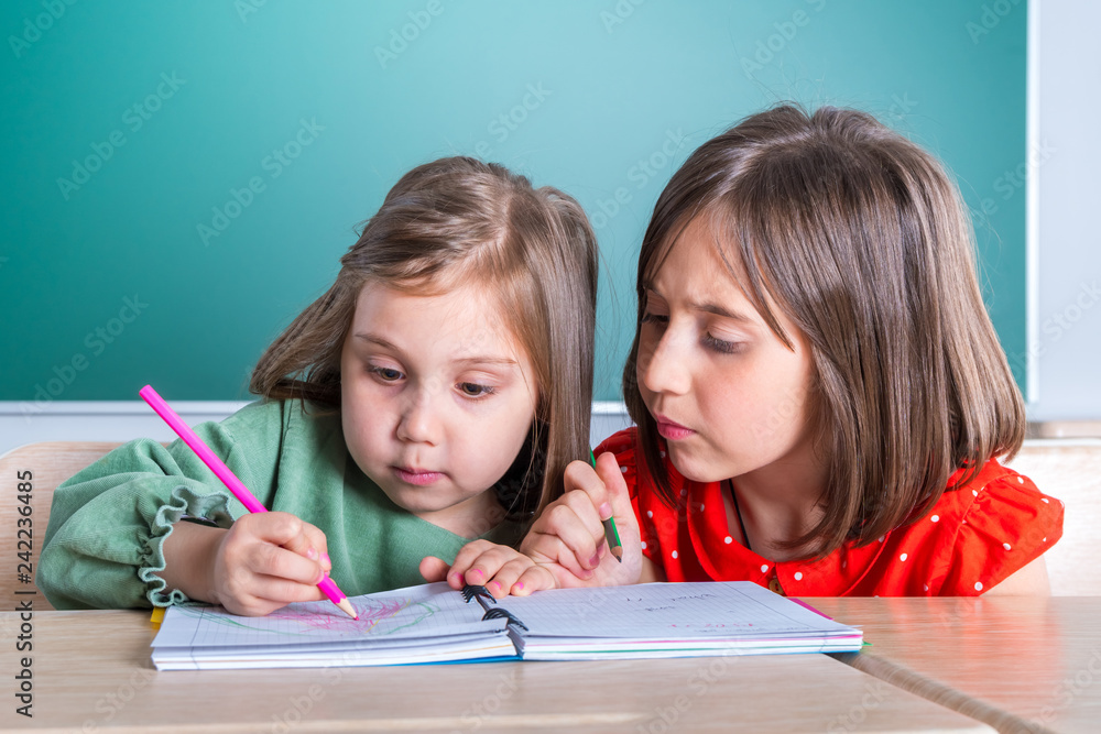 older sister looks at her younger sister as she draws in a notebook older sister looks at her younger sister as she draws in a notebook