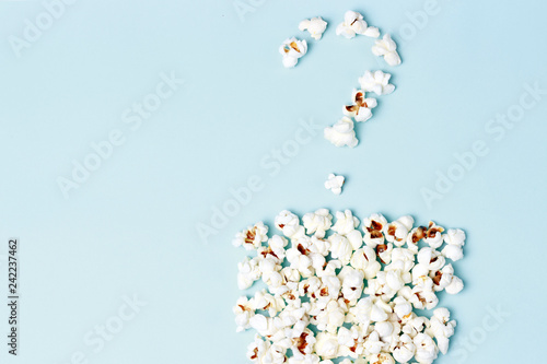 Question mark laid out of popcorn on a blue background close-up, top view, texture