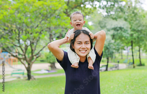 Beautiful young Asian mother with happy baby boy riding on mom's shoulder in the nature park.