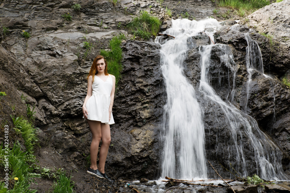 Girl in white summer dress on the background of a waterfall. Girl cold, cold weather and a girl in a dress.
