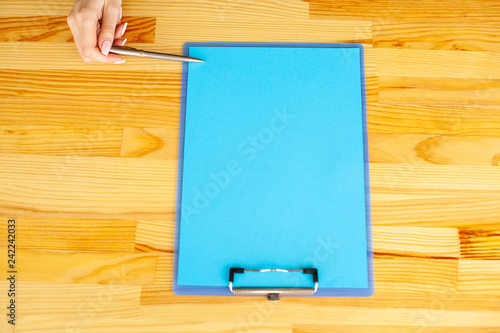 Office Hand Holding a Folder with a Blue Color Paper and Pen on the Colored Background of the Wooden Table. Copyspace. Place for Text