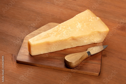 A piece of aged Parmesan cheese with a knife on a dark rustic wooden background with copy space
