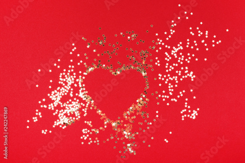 Golden star confetti with shape of heart on red background. Christmas and hol...