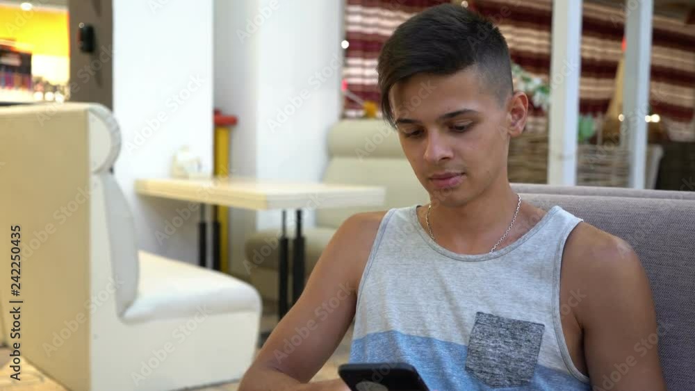 Stylish young man sitting and surfing the net on his phone in a modern cafe Stylish young man sitting and surfing the net on his phone in a modern cafe