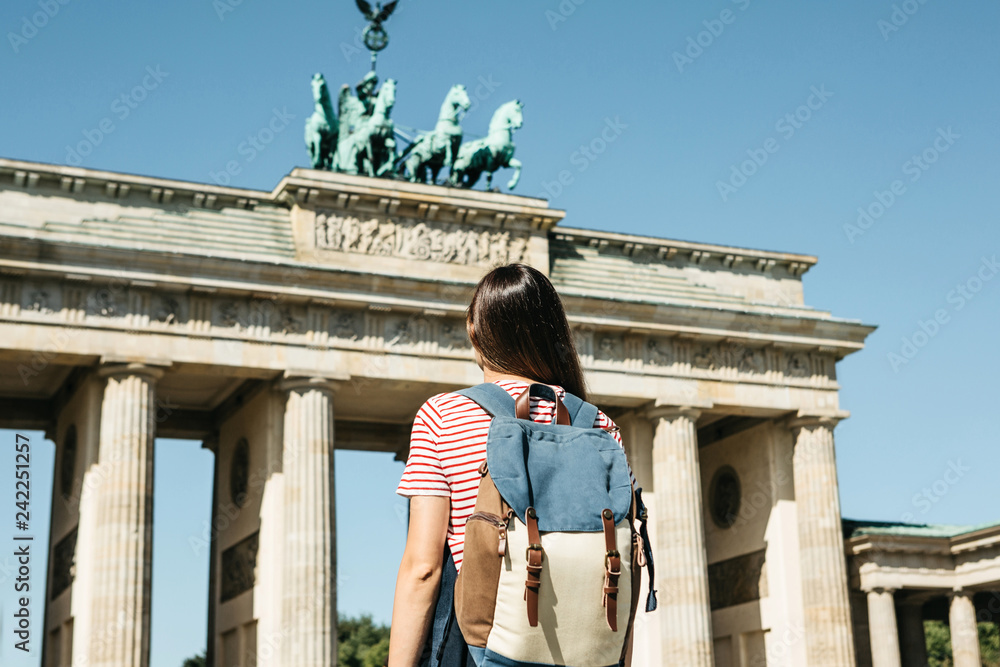 A tourist or a student with a backpack near the Brandenburg Gate in Berlin in Germany, looks at the sights. - obrazy, fototapety, plakaty 