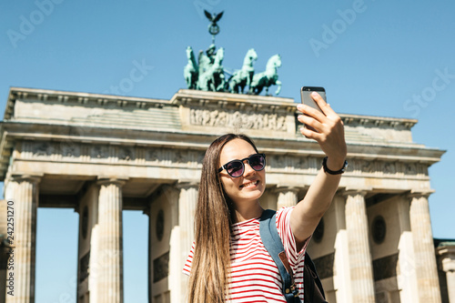 Canvas Print Young beautiful positive girl makes selfie against the background of the Brandenburg Gate in Berlin in Germany or takes pictures of sights