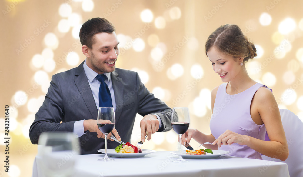 people and leisure concept - smiling couple eating appetizers at restaurant over festive lights on beige background people and leisure concept - smiling couple eating appetizers at restaurant over festive lights on beige background