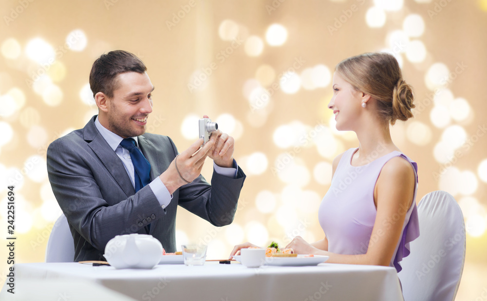 couple, technology and leisure concept - smiling man taking picture of wife or girlfriend by digital camera at restaurant over festive lights on beige background couple, technology and leisure concept - smiling man taking picture of wife or girlfriend by digital camera at restaurant over festive lights on beige background