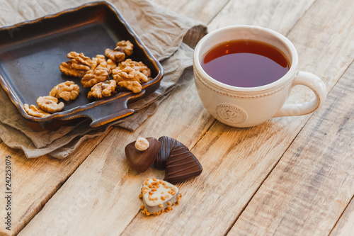 Cup of hot black tea with chocolate candy and walnuts on wooden table, selective focus