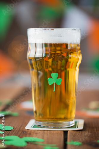 st patricks day, holidays and celebration concept - close up of glass of light beer with shamrock decoration on wooden table