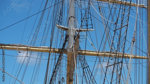 Tall ship rigging gently swaying, frontlit against a blue sky and few clouds. Static shot photo